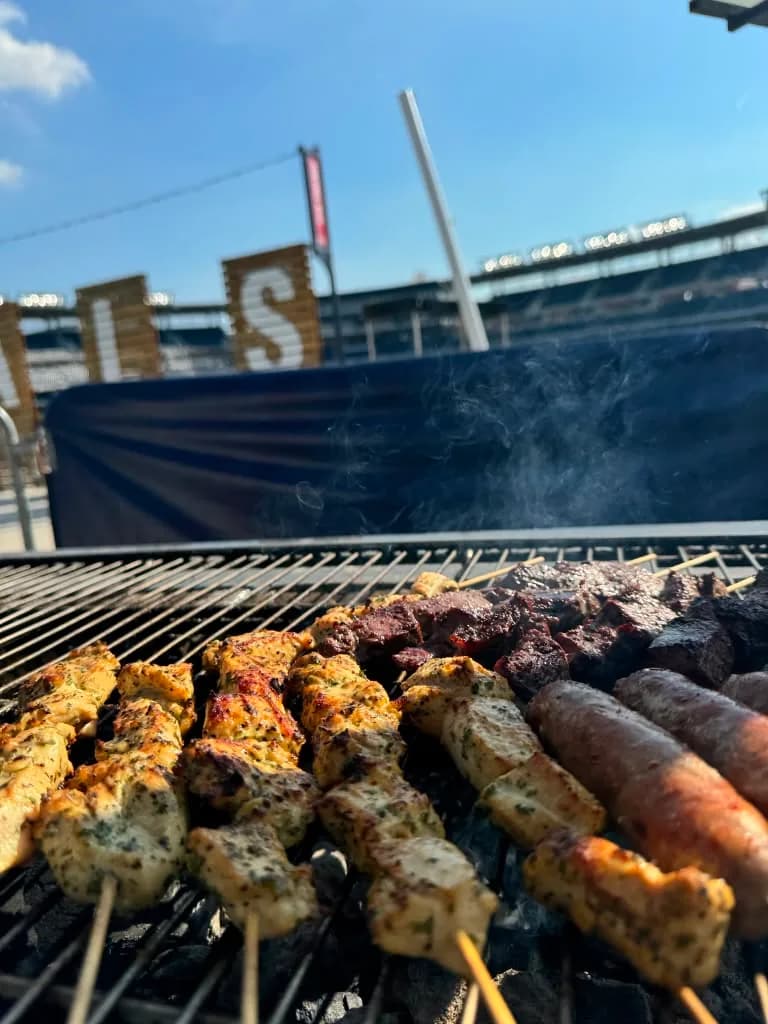 Skewers cooking outdoors beneath a clear blue sky