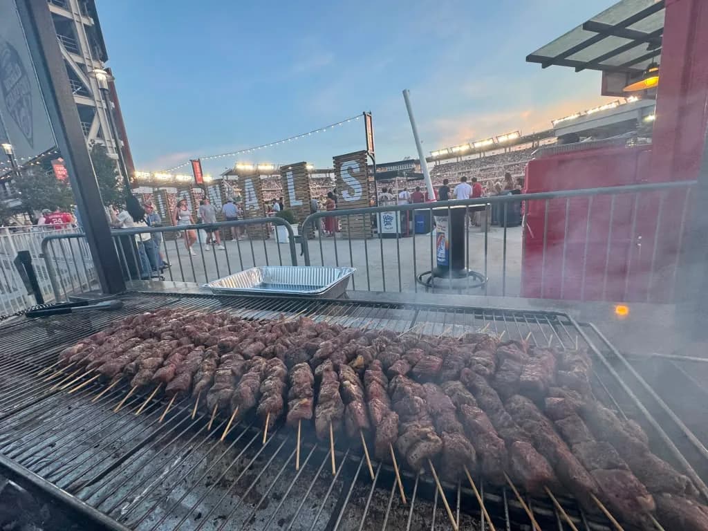 Rows of beef skewers cooking at a busy live event