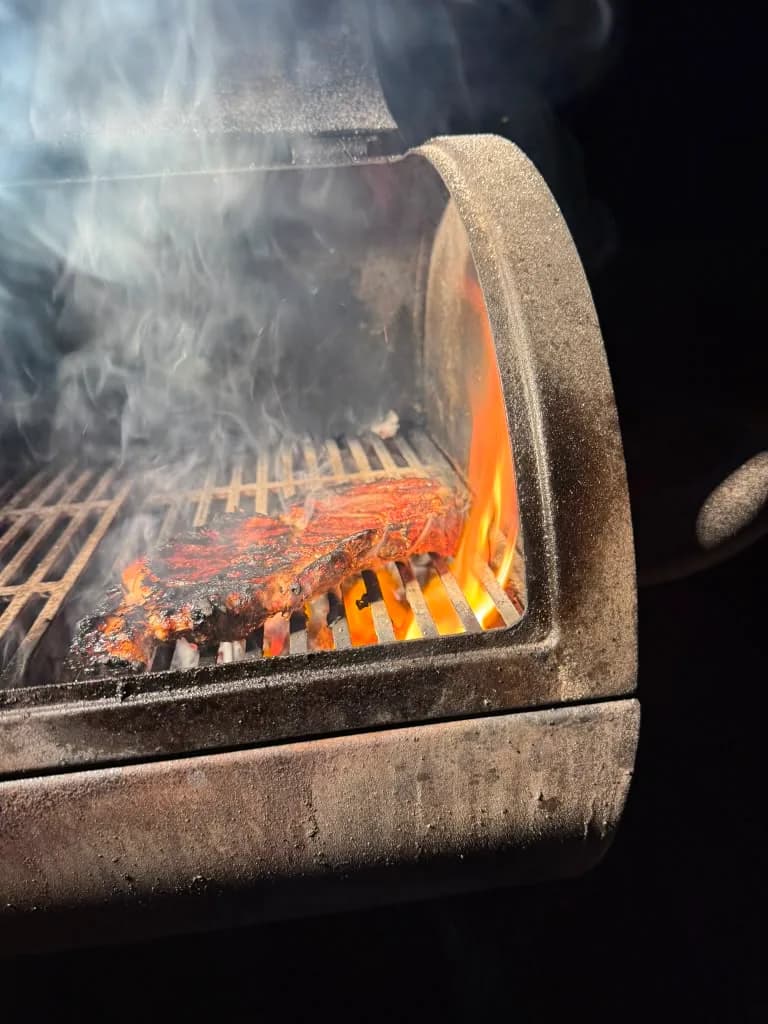 Steak searing beside bright flames and rising smoke
